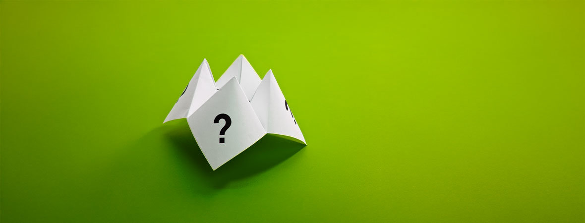 in Papier-Faltspiel mit aufgedruckten Fragezeichen liegt auf einem grünen Hintergrund – Symbol für Unentschlossenheit und Entscheidungsfindung.